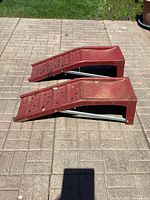 Side view of two red Mastercraft metal car ramps showing incline and support structure.