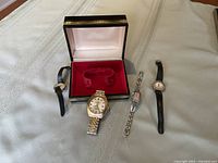 All four watches shown including the men's watch with the presentation box open in the background.