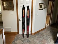 Pair of O'Brien water skis standing upright against a door in a tiled room, showing overall condition and design.