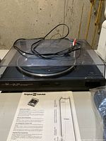 Front view of the Dual CS 515 turntable with closed dust cover. Shows original cables and instruction sheet beside it.