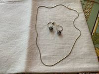 Full view of sterling silver snake chain necklace with lobster clasp and pair of Pandora drop earrings on white cloth background.