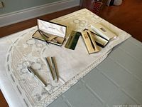 Full lot showing multiple pens and pencil on a white tablecloth: Sheaffer fountain pens, Parker ballpoints, Cross ballpoint pen in box, mechanical pencil.