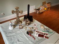 Full view of the religious items laid out on a light green cloth on a floor, including brass cross, bible holder, figurines, rosaries, and other religious artifacts.