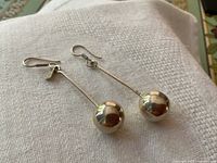 Full view of the pair of long stem sterling silver earrings with ball ends laid on white textured cloth, showing drop length and design.