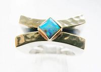 Close-up front view of sterling silver ring with diamond-shaped fire opal in gold setting, showing hammered texture on band.