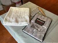 Grey Cuisinart tablecloth and napkin set folded on table with ravioli cutting tray and mini roller