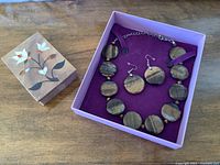 Necklace and earrings inside purple box alongside stone-lidded trinket box on table