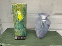 Two decorative vases shown side by side; one tall cylindrical with green, blue, turquoise mottled glaze and one traditional purple swirl vase