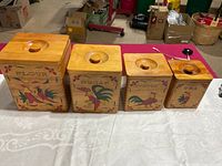 Photo showing all four wooden canisters labeled Flour, Sugar, Coffee, and Tea with hand-painted roosters and floral decorations on the fronts, with round knob lids.