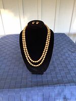 Front and full view of the two strand gold coloured faux pearl necklace and matching earrings on black display stand.