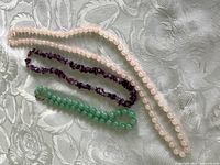Three gemstone necklaces displayed on a patterned fabric showing the amethyst chip choker, rose quartz round bead necklace, and pale green jade bead choker.