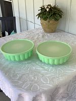 Pair of vintage mint green Tupperware Jell-O moulds with lids displayed on a lace tablecloth.