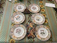 Full view of the set showing six Wedgwood sandwich plates arranged around an enamelled napkin holder on a patterned tablecloth.