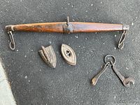 Antique whipped tree 34 inches long with hand forged iron hooks, sad iron without handle and additional old iron tools on iron ring laid out on black pavement.