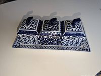 Front angle view of three square ceramic condiment jars with lids and handles on rectangular tray, showing blue and white pattern.