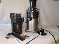 Photo of the Breville Juice Fountain Juicer main unit, pulp container, juice collection jug, power cord, juice outlet cover, and instruction manual arranged on a white background.