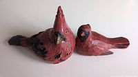 Two hand carved painted wooden cardinals shown side by side on white surface.