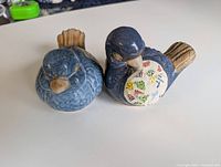 Pair of blue glazed ceramic bird figurines on white surface, showing full shape and color