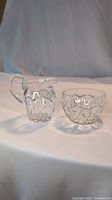 Crystal creamer pitcher and sugar bowl set on white fabric, showing cross and olive pattern details