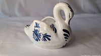 Side view of white ceramic swan with blue floral pattern on the side.