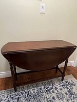 View of the wooden dropleaf table folded with leaves down forming a narrower table with rounded edges and turned legs.