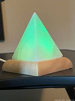 Pyramid-shaped Himalayan salt lamp glowing green on wooden base, USB cable attached.