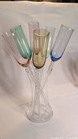 Full set of six multi-colored champagne flutes resting in clear glass vase, shown at front angle.