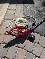 Photo of the red handheld Black and Decker pressure washer with attached white hose and separate rechargeable battery.