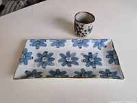 Top and angled view of the rectangular tray decorated with blue painted flowers with a small matching square cup