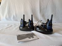 Three Motorola walkie talkies on two black dual charging docks with power supplies, instruction manual in front.