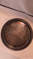 Full view of round sterling silver tray showing tarnish and detailed engraving.