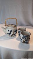 Photo showing the Japanese ceramic teapot with a wooden/reed handle and three matching small cups painted with blue leaves and flowers.