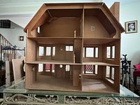 Interior view of large wooden vintage dollhouse showing partitioned rooms, stairs, and extensive window openings.