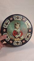 Top view showing the round tin lid with a detailed illustration of a child holding a dog, decorated with floral and heart motifs around the edge.