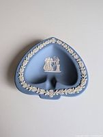 Top view showing spade shape and detailed white relief decoration of two archers with flaming altar, surrounded by white floral garland.