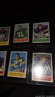 Photo showing 6 of the vintage 1963 Topps football trading cards, each in clear protective sleeves, featuring players Don Goodwin, Jerry Reichow, Pervis Atkins, Bill Savage among others.