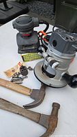 Black & Decker sander with visible wear, router, hammer, bits, and accessories arranged on table.