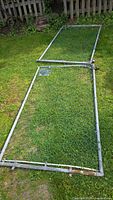 Photo showing two rectangular metal framed chain link fence gates lying on grass, providing overall condition and size perspective.