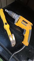 Front view of yellow and black DeWalt DW272 electric screwdriver with attached cord and claw hammer beside it on a dark surface.
