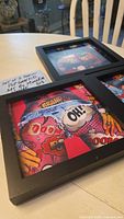 Three framed pop art prints displayed on a table, showing colorful comic and graffiti style themes inside black wooden frames