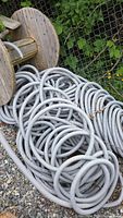 Coil of gray corrugated plastic tubing laid on ground with wooden spools in background