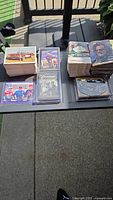 Photo showing multiple stacks of NASCAR and motorcycle racing trading cards arranged on a table outside. Cards include portraits of racers, racing action shots, and various designs, some in plastic sleeves.