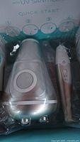 Photo of the packaged silver electric toothbrush and its UV sanitizer unit inside the box, visible through plastic packaging.