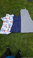 Three dresses laid out on grass: gray long maxi dress, navy blue tiered mini dress, white floral print cold shoulder dress.