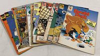 Photo showing 15 Disney comic books fanned out with visible colorful covers featuring characters like Donald Duck and Chip 'n Dale.