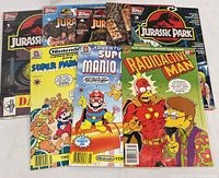 Full group of 8 comic books laid out on white surface showing covers including Jurassic Park, Super Mario, and Simpsons Radioactive Man