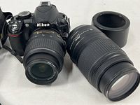 Front-angle view of Nikon D3100 body with 18-55mm lens mounted and 55-300mm lens beside it