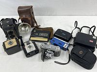 Wide shot of the lot showing all vintage Kodak cameras and accessories, including cases and a flash reflector