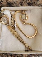 Two wristwatches in white display box, overview of both items