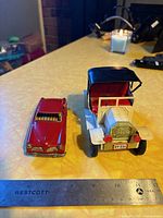 Red and cream vintage metal toy cars placed on a table with a ruler for scale